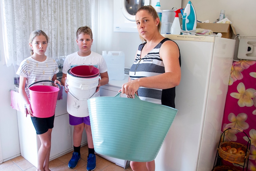 Rebecca Zanatta with her children Jaydon and Macy, hold buckets in the laundry of their home in Stanthorpe.