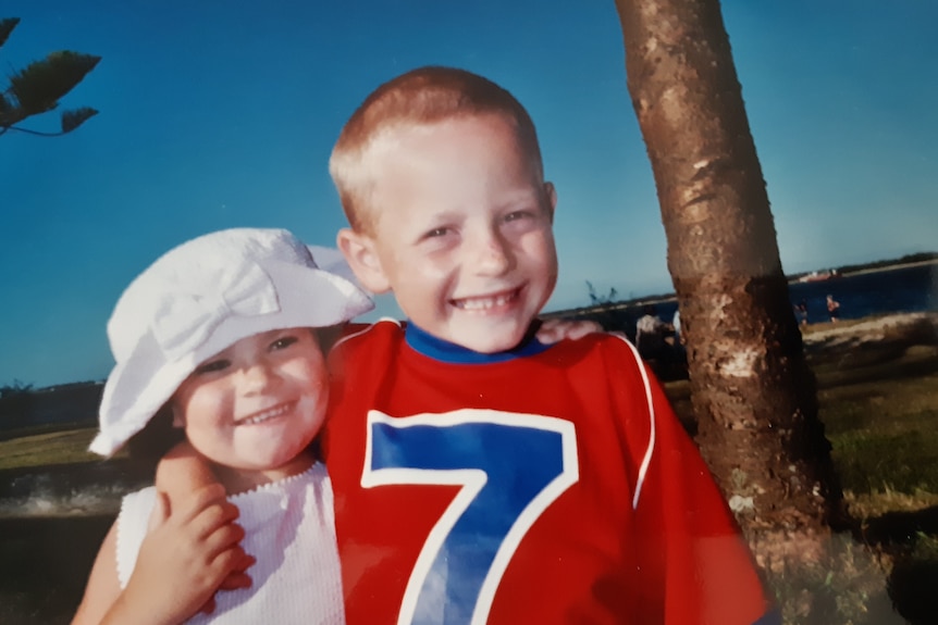 An old photo of two smiling kids at the beach, their arms around each other.
