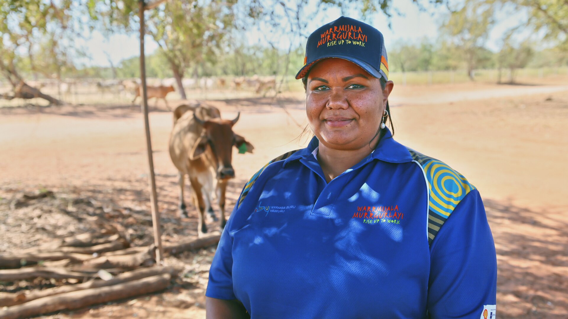 a woman stands looking at the camera with a cow behind her