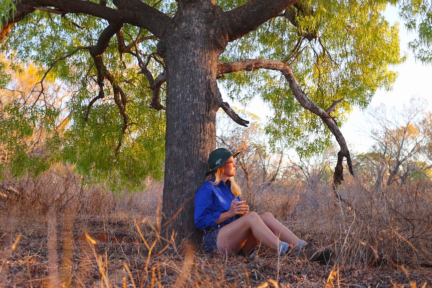 A young lady relaxes with a cup of tea in the shade of a Kurrajong tree