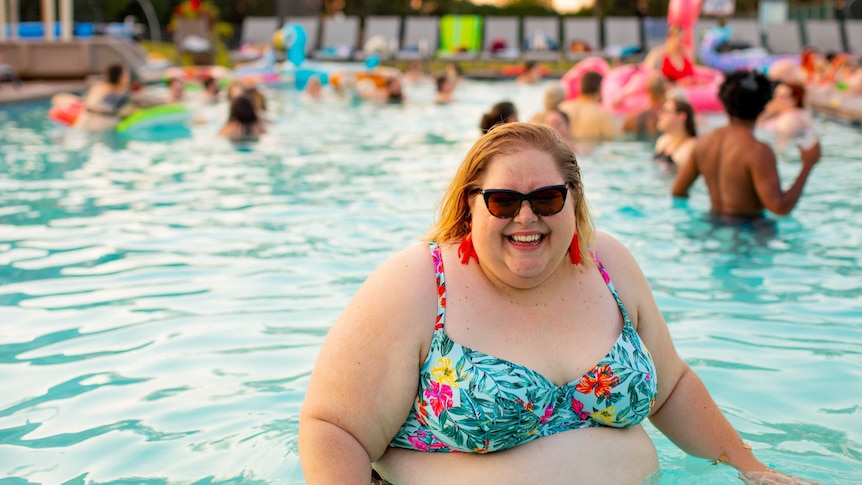 A large woman in a swimming pool wearing sunglasses and smiling for a story about the health impacts of weight stigma.