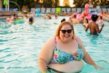 A large woman in a swimming pool wearing sunglasses and smiling for a story about the health impacts of weight stigma.