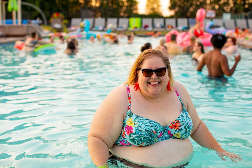 A large woman in a swimming pool wearing sunglasses and smiling for a story about the health impacts of weight stigma.