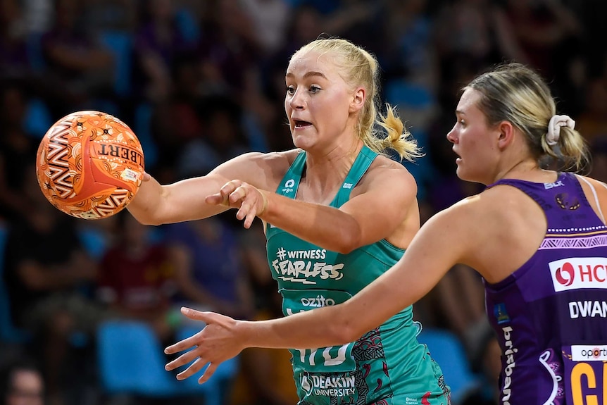 A Super Netballer passes the ball away from her body as opposition player reaches out to stop her.