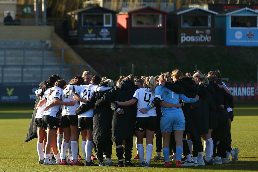 A soccer team wearing black and white stand in a circle after a game with some huts in the background