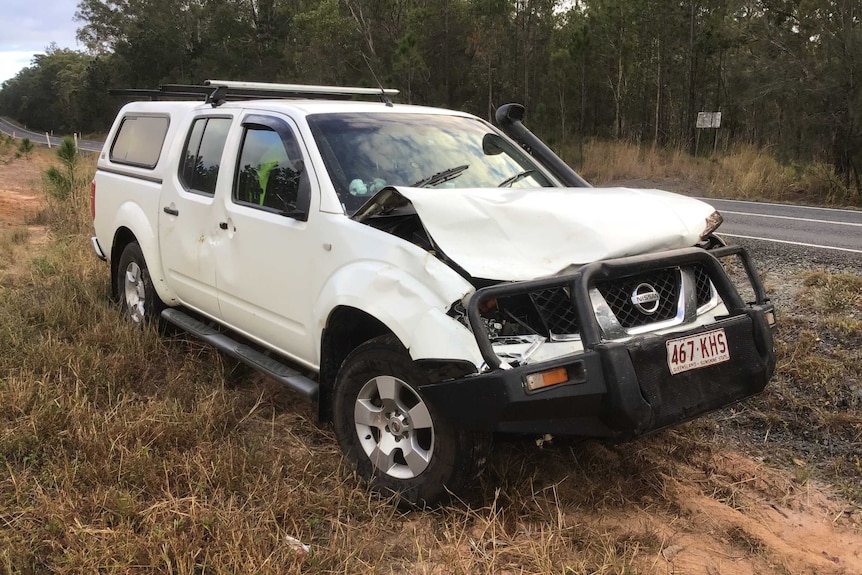 A white dual-cab ute parked on the side of a rural road with its bonnet crushed after a head-on collision.