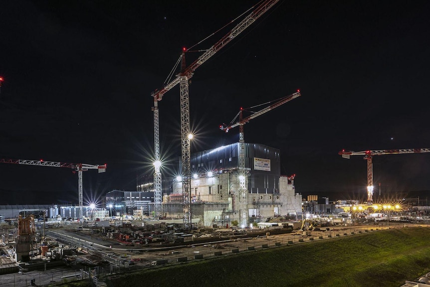 Le gru sorvolano l'edificio principale di ITER, illuminato di notte