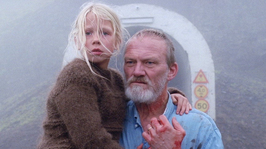 An older man covered in blood, holding a young girl standing in front of a tunnel on a foggy day in the film A White, White Day