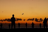 Silhouettes of people standing on a beach at sunrise.