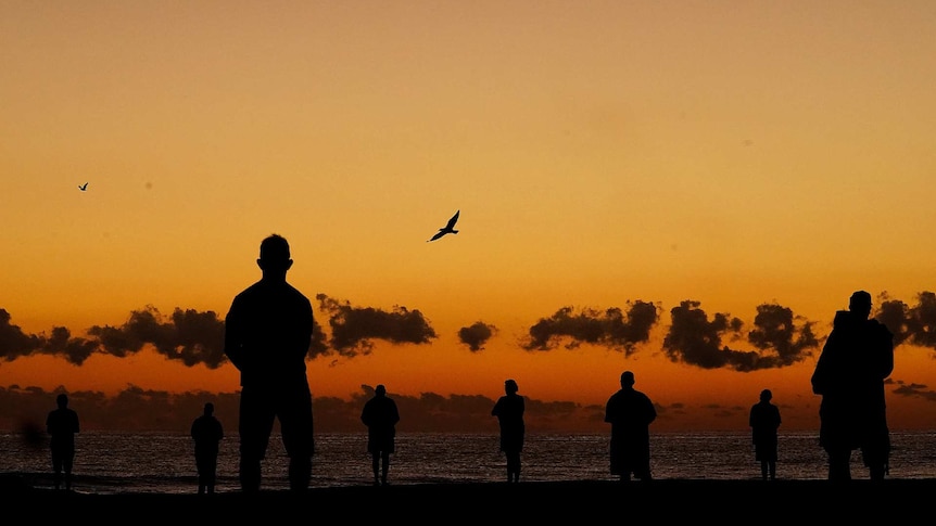 Silhouettes of people standing on a beach at sunrise.