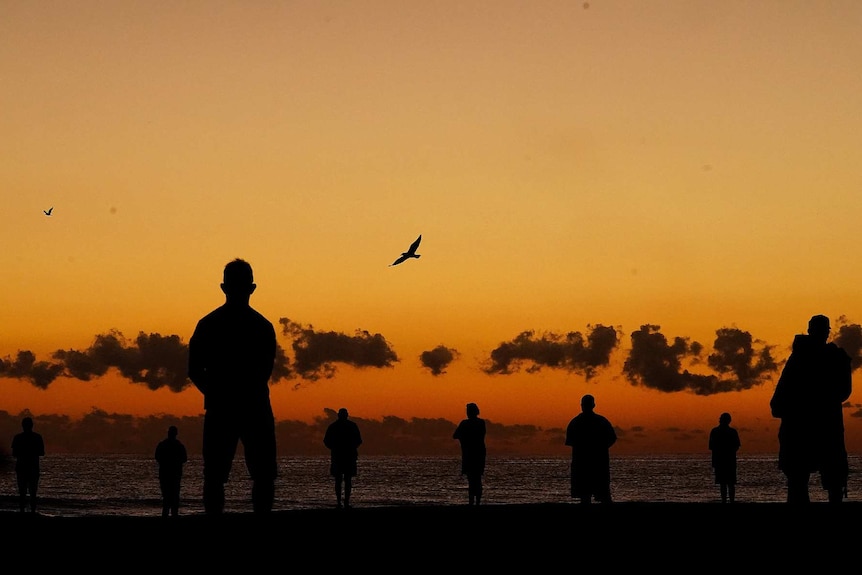 silhouettes of people standing on a beach at sunrise