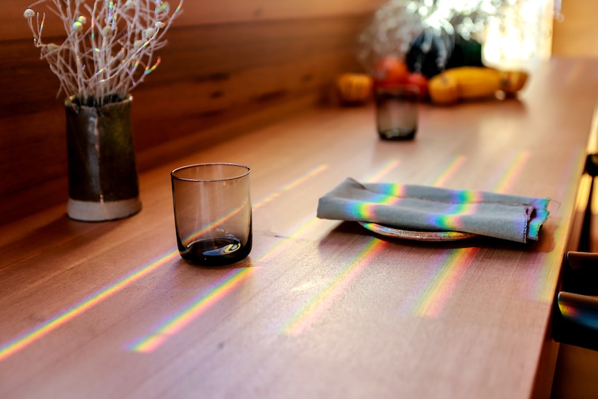 Light reflects across a restaurant wooden dining table with a glass and napkin sitting beneath the light