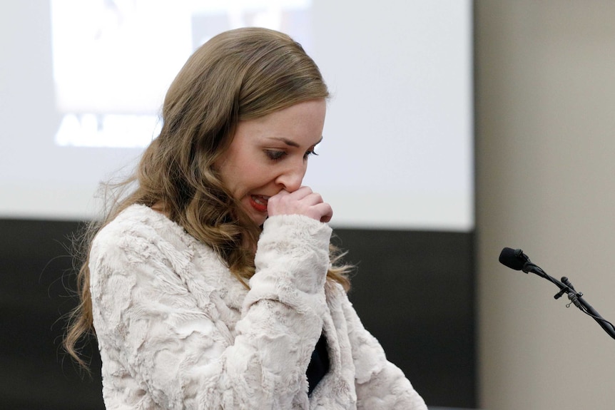 A young woman wipes her nose while speaking into a microphone.