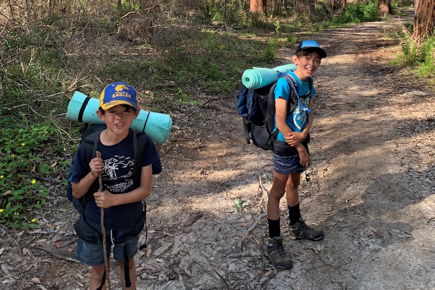 two boys with backpacks in front of a forrest