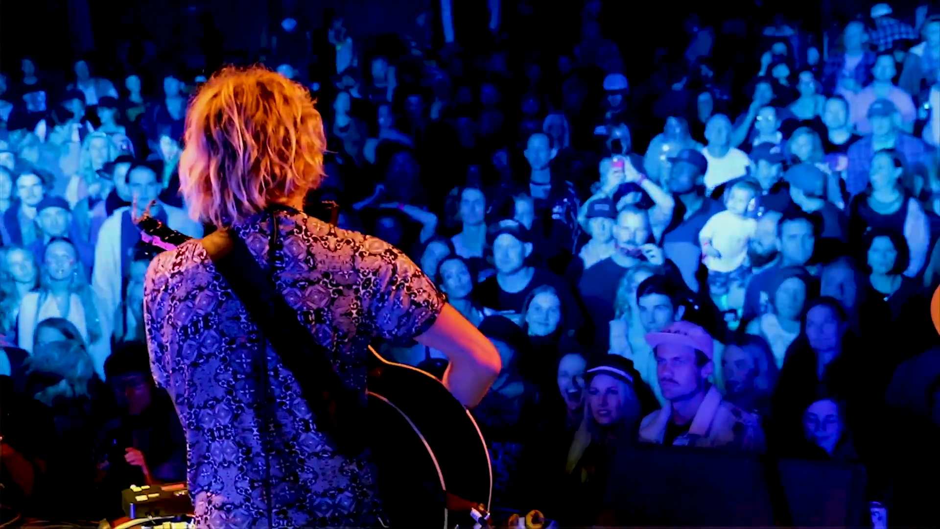 A sea of faces watching a single male viewed from behind playing a guitar