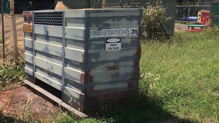 A metal box with a sign saying high voltage sits in an industrial-looking area.