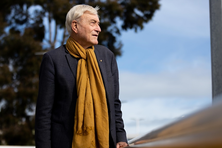 An elderly man in winter clothing stands next to the railing on a bridge.