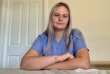 Caitlin Bourke wearing her clinical scrubs leaning her crossed arms over her bed