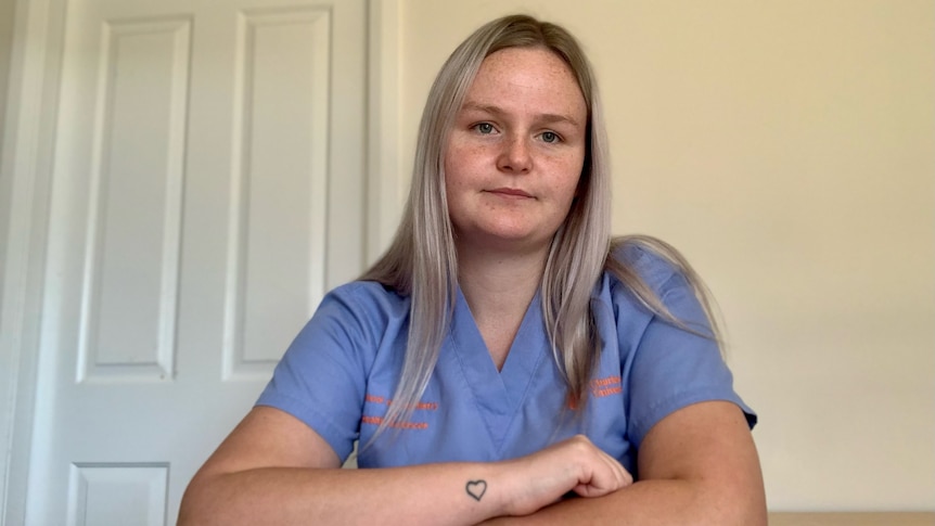 Caitlin Bourke wearing her clinical scrubs leaning her crossed arms over her bed