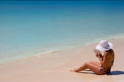 A woman sitting on the beach reading a book.