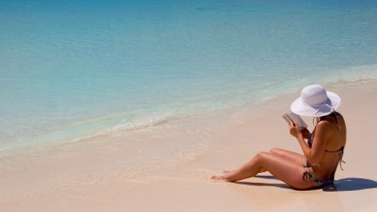 A woman sitting on the beach reading a book.