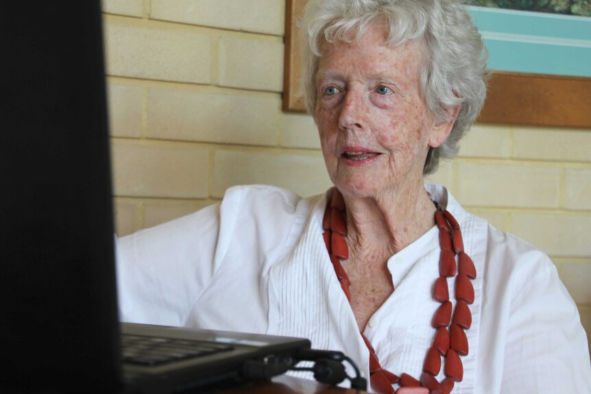 An elderly woman looks at a computer screen.