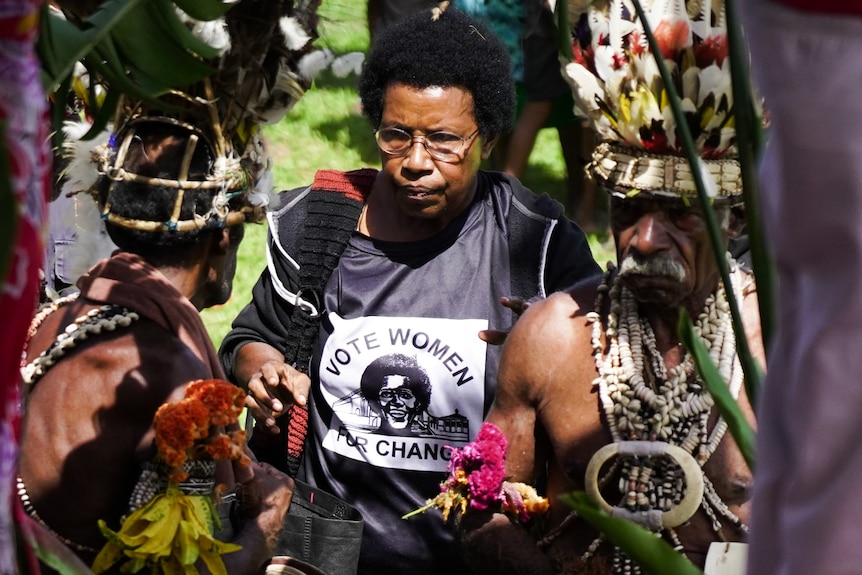 A woman wears a black Tshirt with 'VOTE WOMEN FOR CHANGE' slogan. Men are in traditional PNG dress