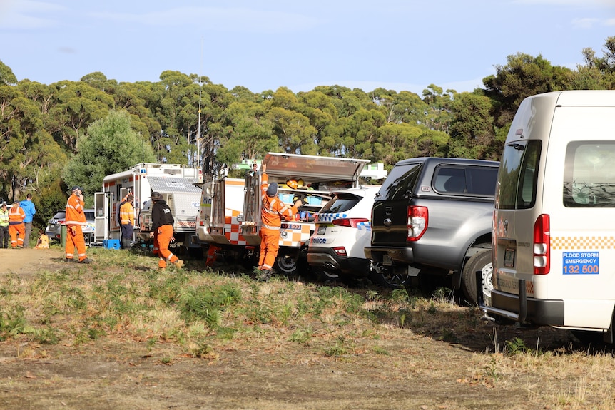 Search crews and vehicles parked in a row on a field.