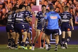 A Cowboys NRL player runs to celebrate with a trainer as his teammates hug after a finals victory.