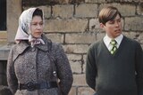 A young Queen Elizabeth II, wearing a scarf tied around her hair and secured under the chin, with then-teenaged Prince Andrew