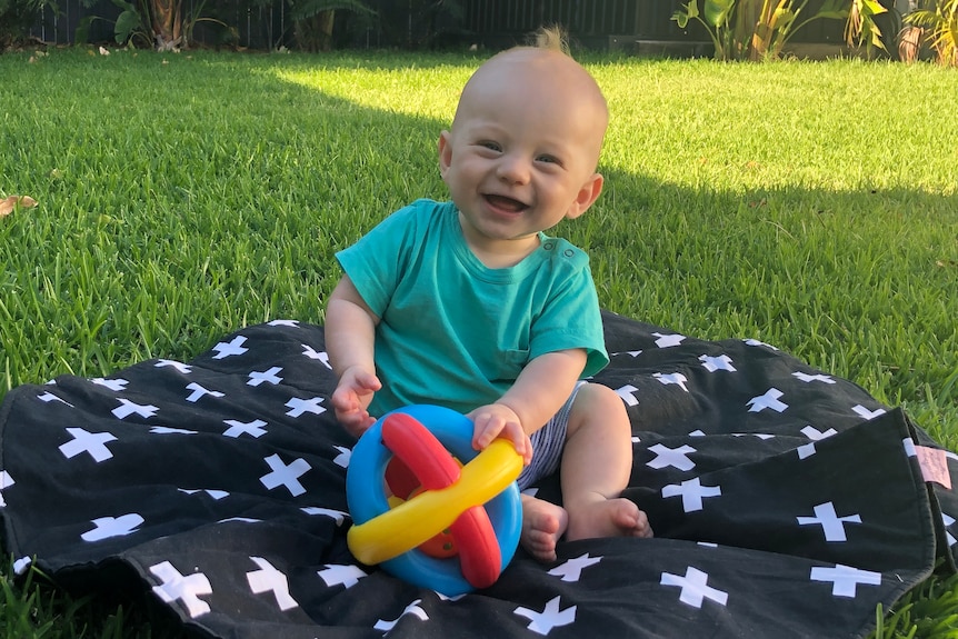 a baby sitting on a blanket laughing with a toy
