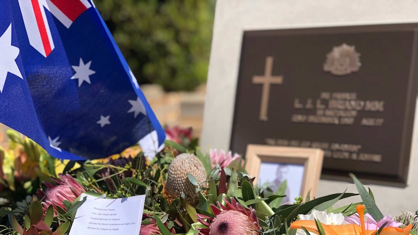 Wreaths of flowers and the Australian flag at a war memorial headstone