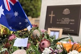 Wreaths of flowers and the Australian flag at a war memorial headstone
