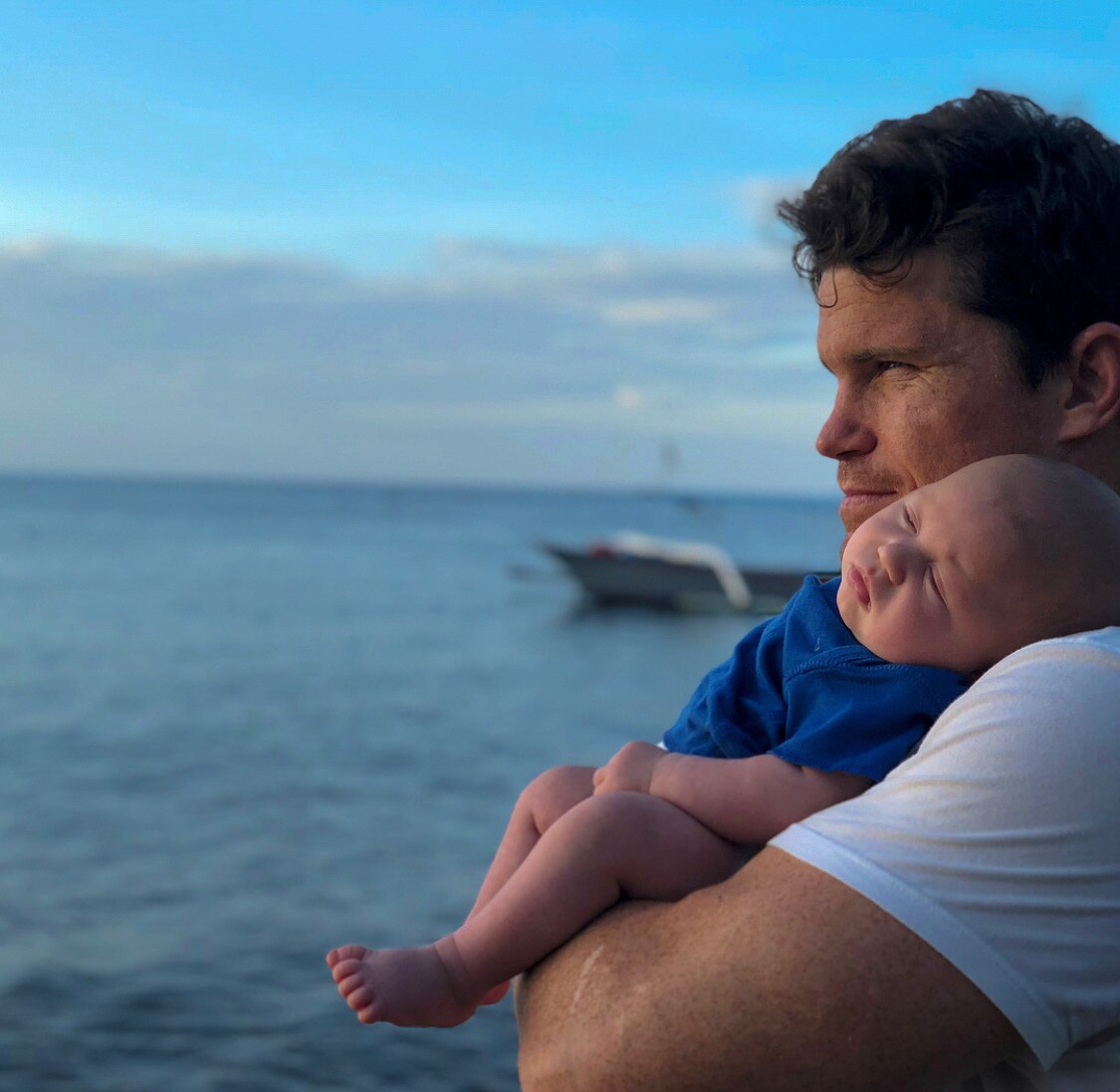 A man holding his baby while looking over an ocean