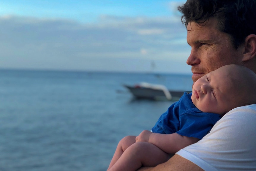 A man holding his baby while looking over an ocean