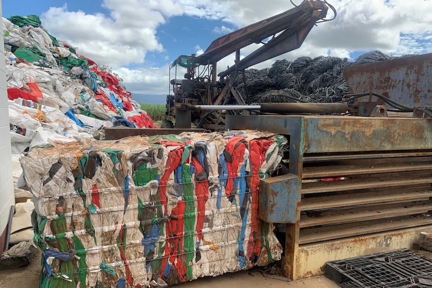 A giant cube consisting of melded together and colourful pieces of plastic sits in front of some machinery.