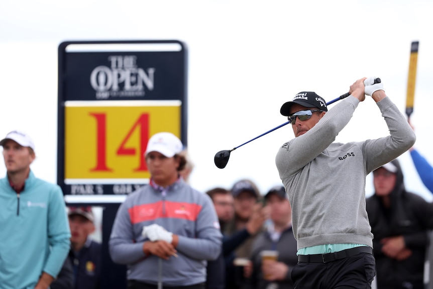 A sweater-wearing golfer hits off the tee with a sign saying "The Open, 14" in the background. 