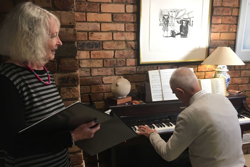 A couple sing together beside a piano.