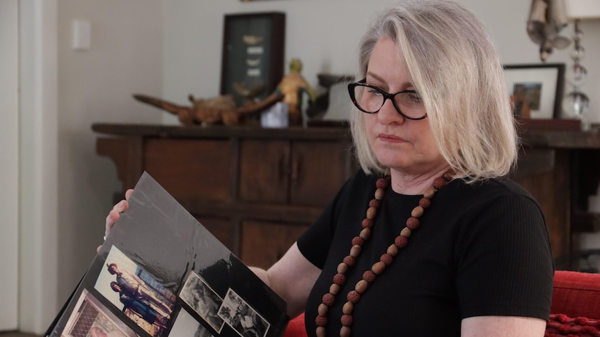 A sad-looking woman seated on a couch looking through a photo album, 