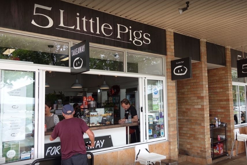 A man lines up for takeaway coffee outside a cafe called 5 Little Pigs.
