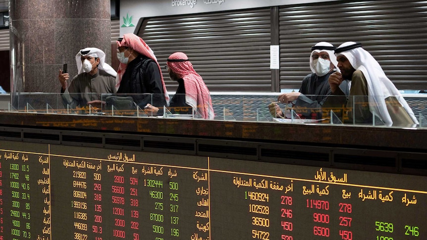 Traders wearing protective masks stand above a screen displaying stock prices.