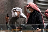 Traders wearing protective masks stand above a screen displaying stock prices.