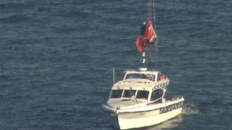 person suspended from cables being lowered onto boat