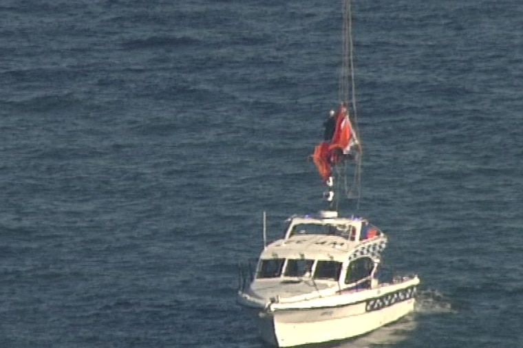 person suspended from cables being lowered onto boat