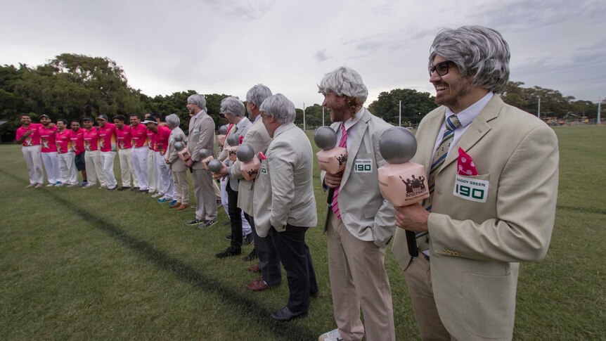 A line of men in pink shirts and men in silver wigs with bone blazers.