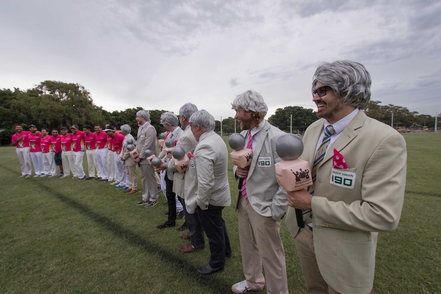 A line of men in pink shirts and men in silver wigs with bone blazers.