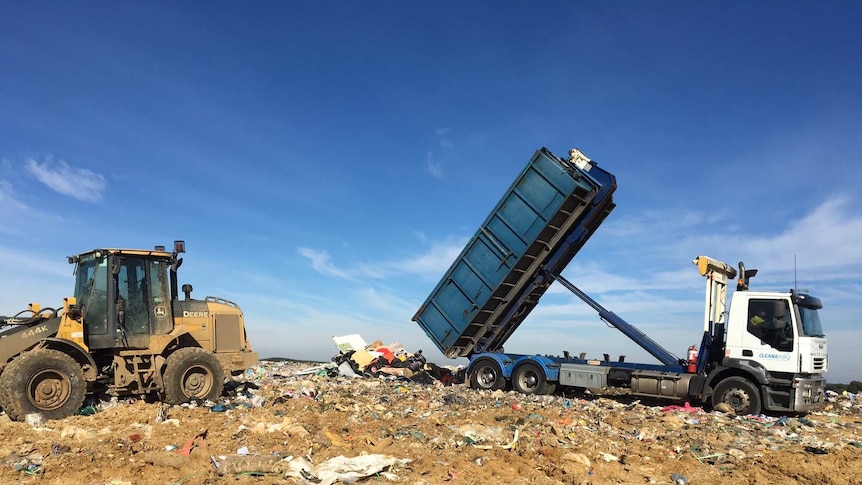 A tractor and truck dump rubbish on a heap.