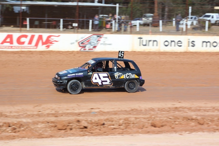A black car racing around a dirt track.