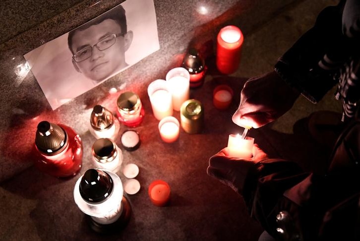Journalist lights a candle to place in a small memorial with picture of Jan Kuciak