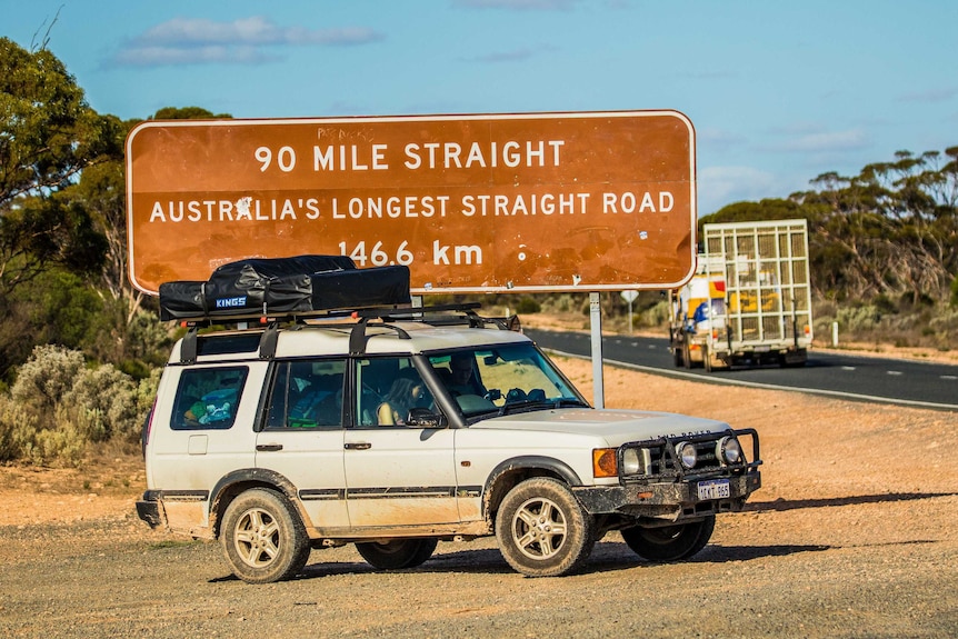 A four-wheel-drive vehicle and truck near a road sign on the remote Nullarbor.